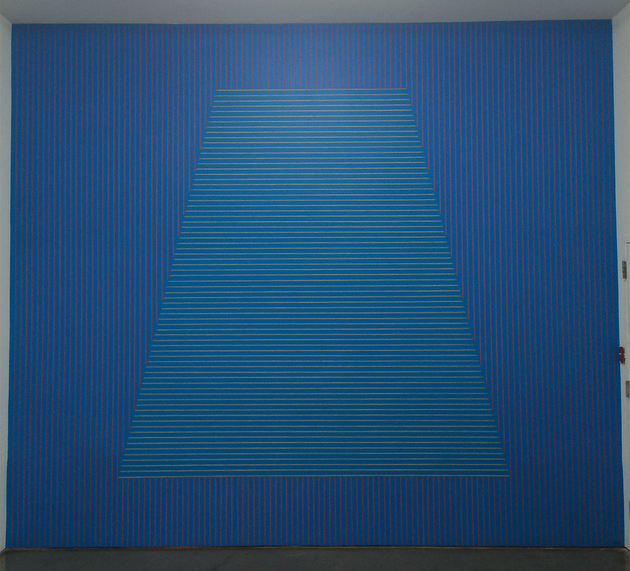 Sol LeWitt, "#333: On a blue wall, red vertical parallel lines, and in the center of the wall, a trapezoid within which are yellow horizontal parallel lines. The vertical lines do not enter the figure" (May 1980) at Gladstone Gallery
