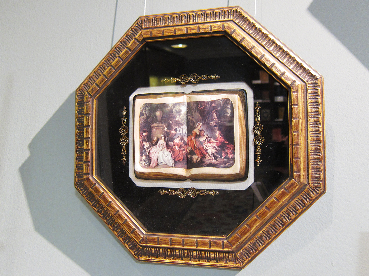 A framed faux box with three-dimensional open books showing decoupage images of famosu European paintings (mid-20th c.) 