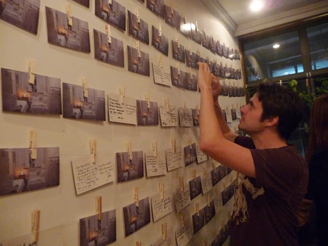 A visitor photographs his postcard after hanging it up on the wall.