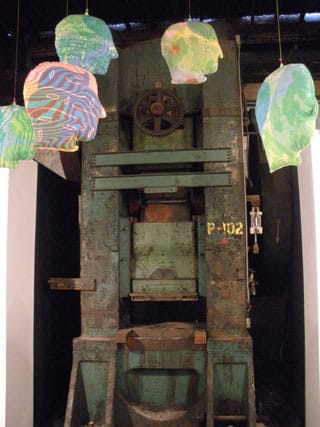 Sculptures by Mike Perry hang in front of an old piece of machinery in the space