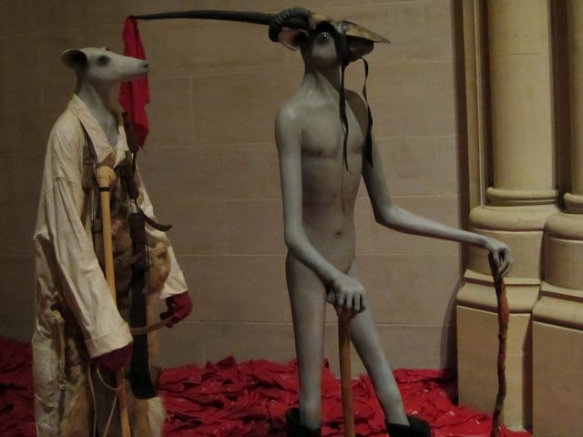 Jane Alexander, "Ghost" (2007), fiberglass, oil paint, found clothing, carved alien-wood knobkerrie, rooikat (caracal) pelt, lacing, machetes, sickles, gloves, rubber boots; and "Harbringer with protective boots" (2004), fiberglass, oil paint, carved wood walking sticks, rubber boots, gemsbock horns, rubber strap, cotton cloth