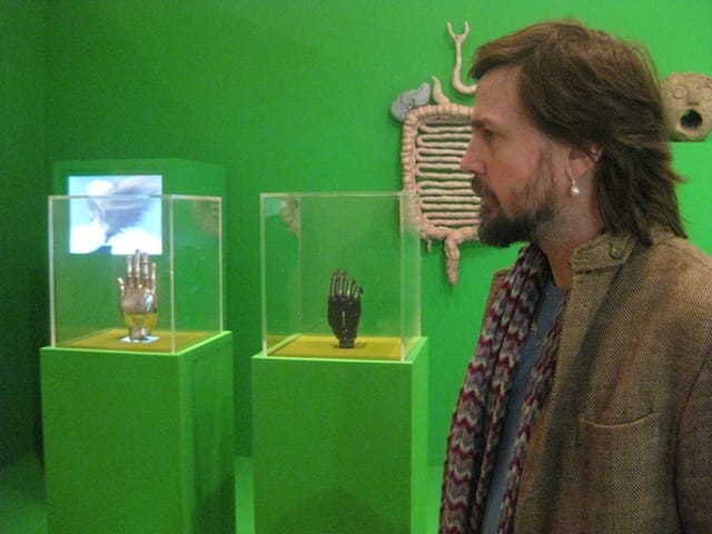 Mark Leckey pictured with displays of bionic hand and silver reliquary (all photographs by the author fo Hyperallergic)