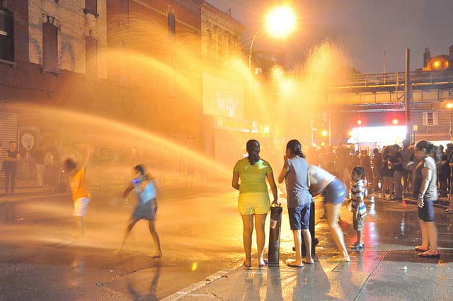 Children playing with an open fire hydrant as performance art fans congregate outside Grace Exhibition Space for the Friday, July 19th program, featuring Ron Athey and others. (all photos by the author for Hyperallergic)