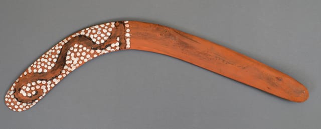 Ceremonial Warlpiri boomerang, freshly made and painted with designs in charcoal, ochre and pipeclay, representing the great Snake Dreaming at the sacred Ngama cave, north of Yuendumu. The boomerang was made and decorated for the performance of the Ngama ceremony which was held during the Uprange Ministerial Expedition of 1971. The aim of the expedition, which was largely the initiative of former South Australian Museum Curator Robert Edwards, was to introduce the importance of Aboriginal heritage sites in South and Central Australia to the Federal and State Government politicians.