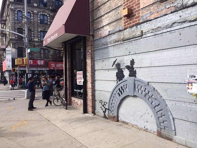 Building supervisor Feliciano Perez being interviewed by a reporter as he stands guard by the Banksy.