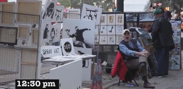 A bored salesman sits in front of his table of "real" Banksys that go unnoticed.