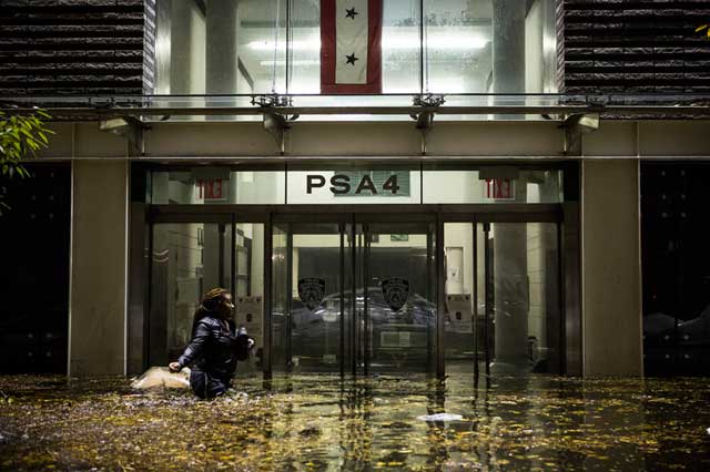 David Maurice Smith, "A female resident of Manhattan's downtown Eastside makes her way past the Police Service Area 4 Station located on the corner of Avenue C and East 8th. The station was the only building in the area with lights, running off of an auxiliary power supply. Officers barricaded themselves inside while the streets flooded with waist deep water. October 30, 2012" (2012) (© Smith/Oculi) (via icp.org)