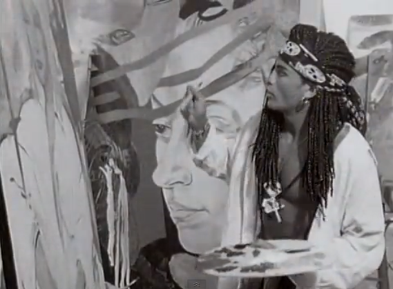 One of the Milli Vanilli duo painting with another painting in the background. (screenshot by the author)