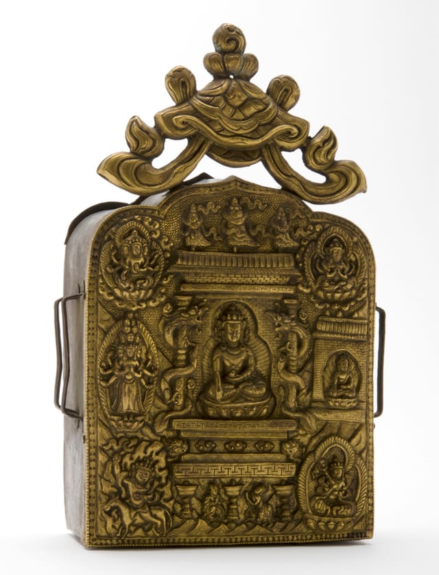  portable shrine containing mantras This large and elaborate gau has brackets on either side through which it was strapped to the waist of a wearer or perhaps tied to a ack animal when travelling. It contains printed mantras on thin paper and its exceptionally elaborate repoussé brass front depicts a seated Aksobhya surrounded by deities including Vairocana, eleven-headed Avalokitesvara and Palden Lhamo (dPal Idan Lha mo). Tibet or Nepal. Height 26cm