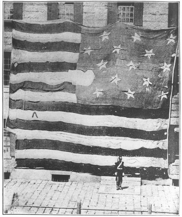 courtesy of the National Museum of American History This, the first known photograph of the Star-Spangled Banner, was taken at the Boston Navy Yard on June 21, 1873, presumably by Commodore George Preble, a naval historian and author of the first history of the American flag, published in 1872.  Preble corresponded with Georgiana Armistead Appleton when he learned she possessed the original Fort McHenry flag. He had her permission to borrow it so that it could be  photographed for the second edition of his book.  Preble found the flag to be too delicate to withstand flying on a flagpole so it was hung from the second story of one of the Navy Yard buildings.  Afterwards, he wrote to Georgiana Armistead Appleton that he "obtained a couple of Marine privates to stand in full dress and be photographed with it to show by comparison its size, and at the same time serve as a guard of honor." (Smithsonian Institution Photo)>