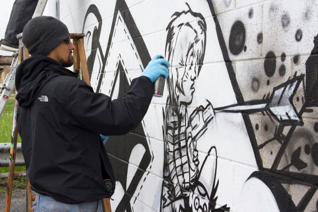 An artist working on the section of the mural that stirred debate, a figure of a young boy with a gun (photo by Nabiha Khan) (click to enlarge)