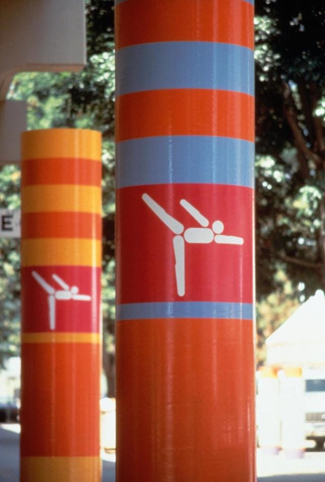 "Look of the Games" on columns, designed by Deborah Sussman (©IOPP / Annette Del Zoppo) Los Angeles 1984 OG, Views and atmosphere of the city - Pictogram of gymnastics at the Pauley pavilion.