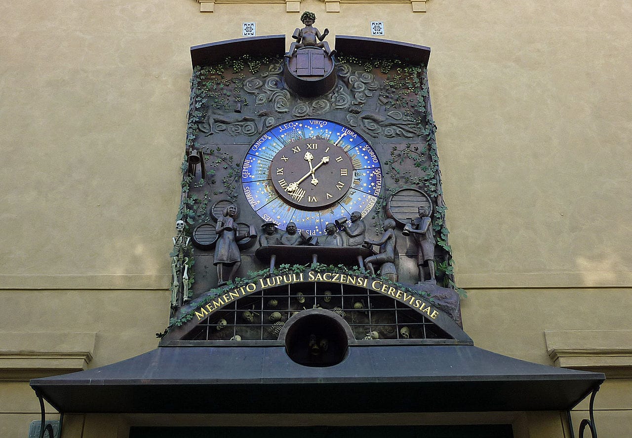 Clock with people drinking at a bar while a cemetery is embedded below, in Žatec, Czech Republic (photograph by SchiDD/Wikimedia)