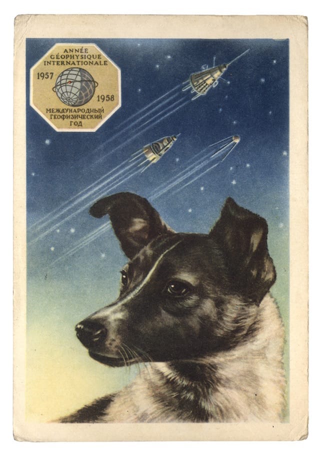Postcard of Laika with the first three Sputniks in the background by artist E. Gundobin, USSR (1958). Text reads: “International Geophysical Year 1957–1958″ (© FUEL Publishing)