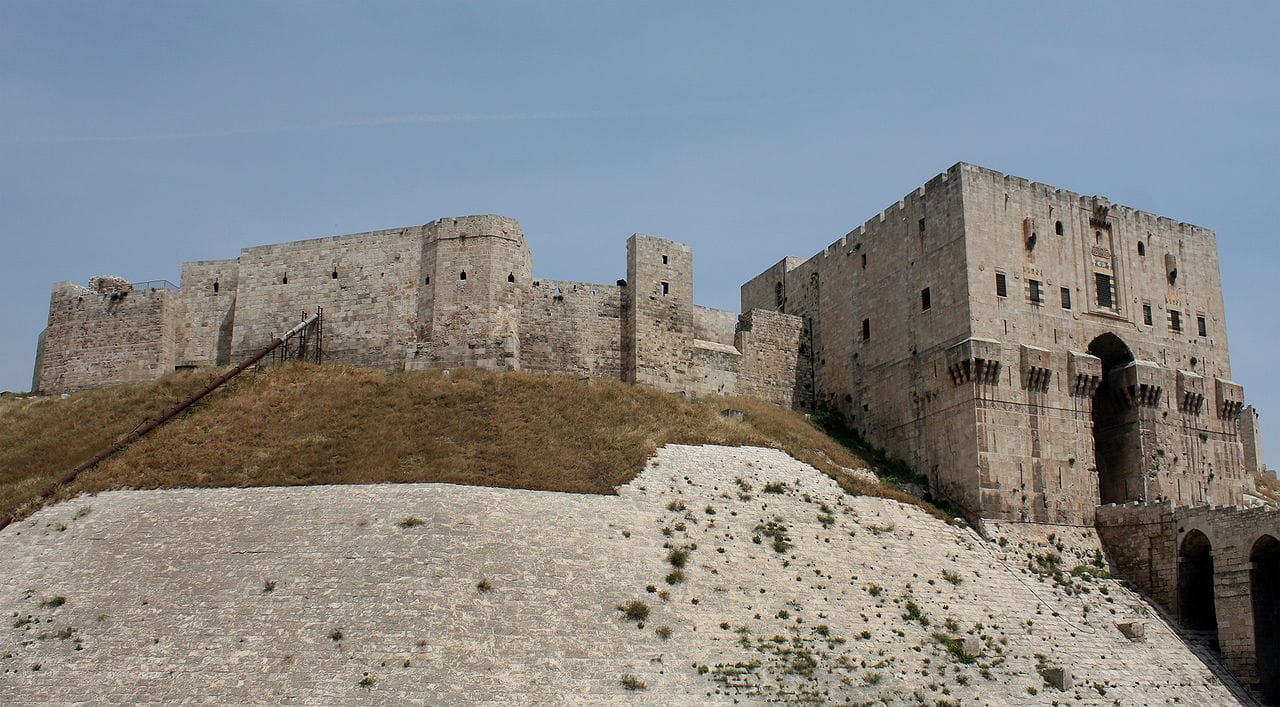 The Citadel of Aleppo, one of many sites damaged by the Syrian Civil War (Image via Wikimedia)
