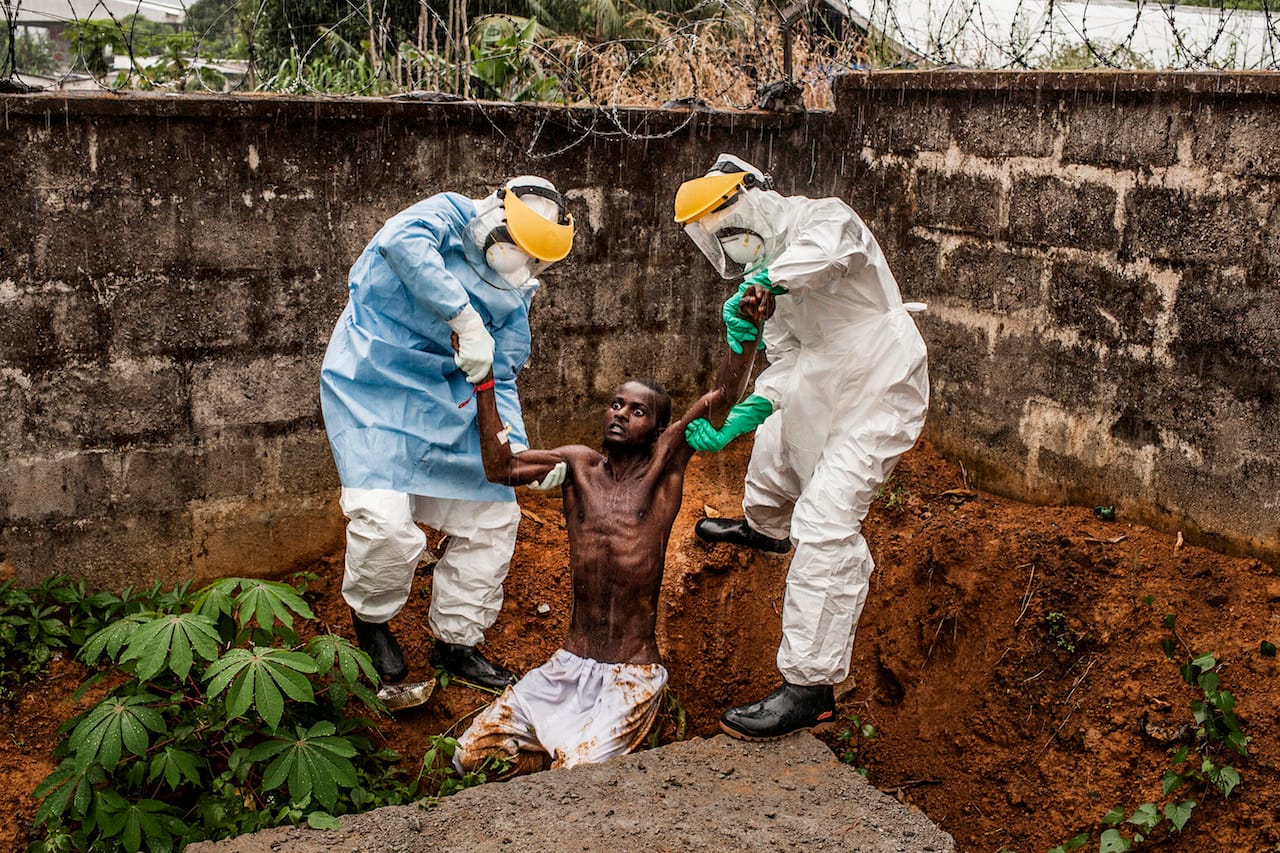 First Prize General News Category, Stories Pete Muller, USA, Prime for National Geographic / The Washington Post Freetown, Sierra Leone Caption: Medical staff at the Hastings Ebola Treatment Center work to escort a man in the throes of Ebola-induced delirium back into the isolation ward from which he escaped. In a state of confusion, he emerged from the isolation ward and attempted to escape over the back wall of the complex before collapsing in a convulsive state. A complete breakdown of mental facilities is a common stage of advanced Ebola. The man pictured here died shortly after this picture was taken.