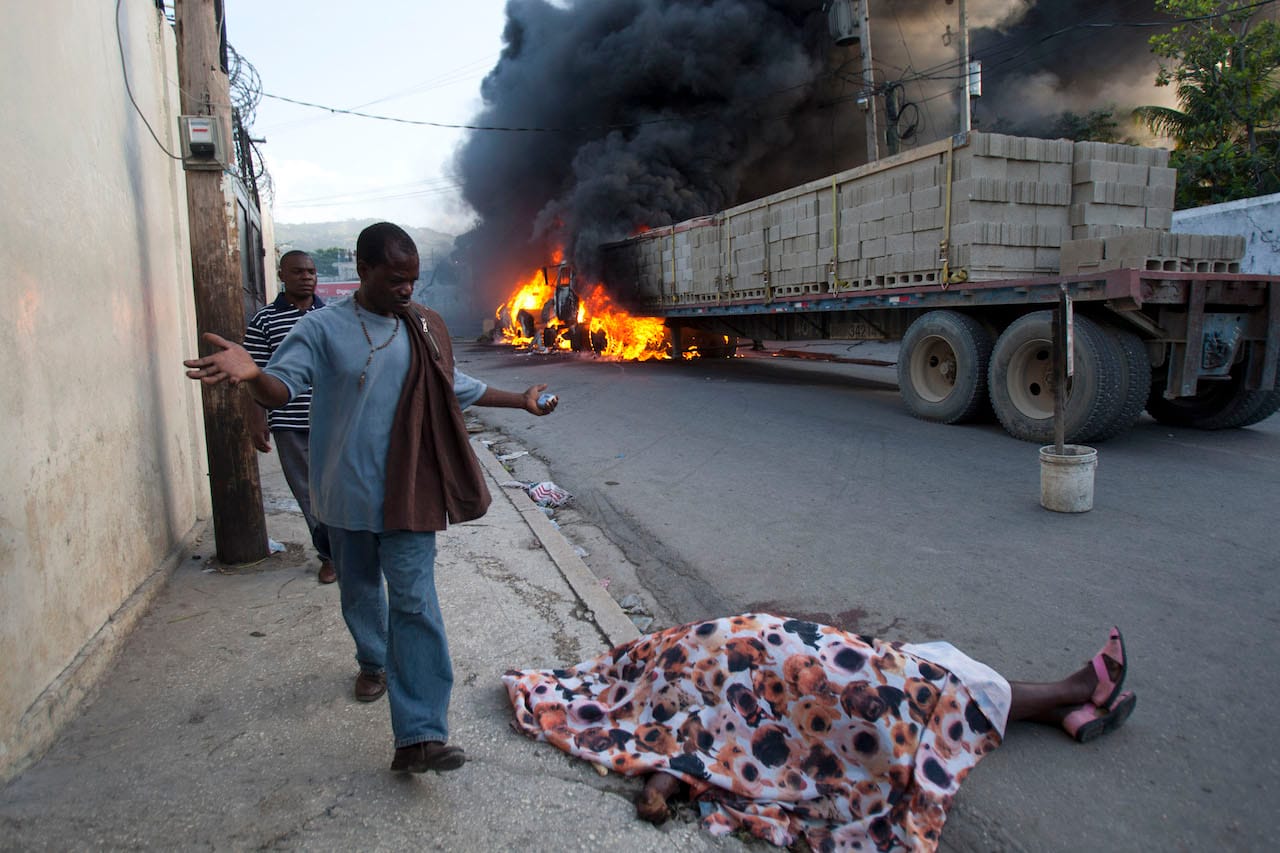 Dasilia Daniel. A resident expressing shock, walks by the body of rice vendor Dasilia Daniel, who was accidentally shot dead during a road rage incident as she walked to work in the Petionville surburb of Port-au-Prince, Haiti, Friday, July 19, 2013. According to Daniel's cousin, Aclite Laurent, the driver of a semi-trailer truck, pictured in background, tapped the back of a pickup, enraging its driver, who then stepped out from his vehicle, gun in hand, and shot at the semi-truck driver, missing him and killing Daniels. Fellow vendors set the vehicles on fire in retaliation for the death of their friend. © Dieu Nalio Chery/ AP Photo.