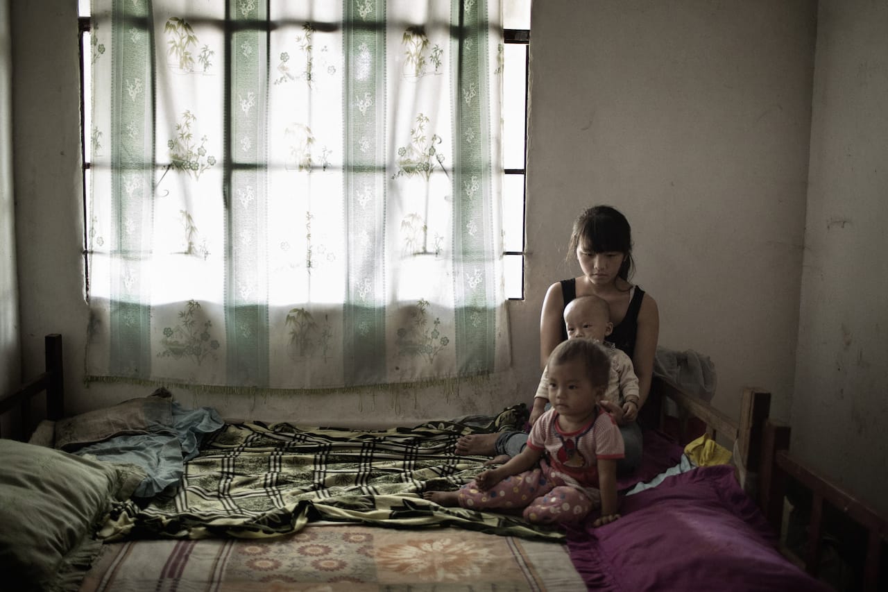 16-year-old Xiao Mei sits on bed with her 2-year-old daughter (front)  and 1-year-old son at home. Xiao Mei and her husband were classmates in primary school. They started dating at sixth grade and dropped out of school when they got married in 2011. Shuichang village, Mengla county, Yunnan province, November 3, 2014. © Muyi Xiao.