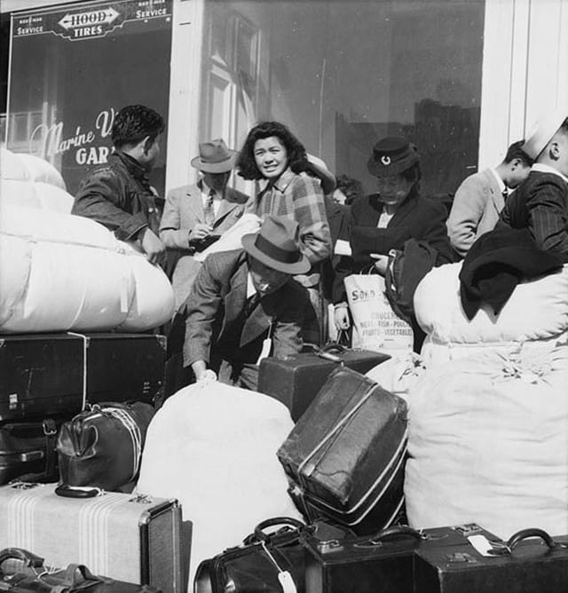San Francisco, April 16, 1942. Americans of Japanese descent from the first contingent of 664 from awaiting buses at Van Ness Avenue to be transported to Santa Anita Park assembly center at Arcadia, California. Photo by Dorothea Lange, WRA / Courtesy of the National Archives (National Archives Identifier 536417)
