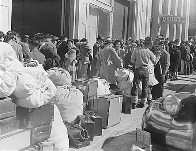 April 6, 1942, San Francisco. Japanese and Japanese Americans await a bus with the belongings they were allowed to bring at the WCCA station on Van Ness Avenue, part of the first group of 664 to be evacuated from the city (Photo by Dorothea Lange, WRA / Courtesy of the National Archives, Records of the War Relocation Authority (National Archives Identifier 536065))