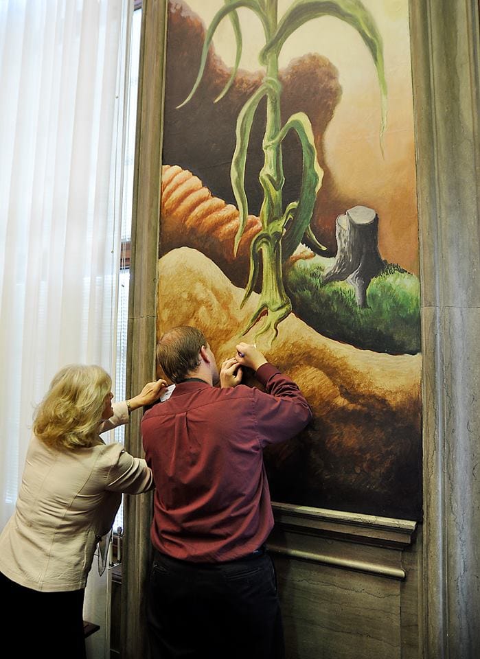 Missouri Republican Party Vice Chairwoman Valinda Freed and an unidentified man writing on business cards while leaning on the Thomas Hart Benton mural (photo by Dave Marner, via Facebook)