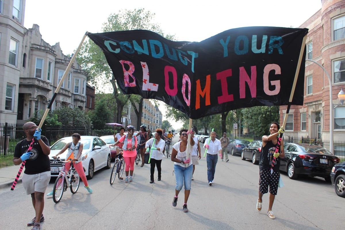 Cauleen Smith and other artists participating in the march lead the way with a banner with the phrase, “Conduct Your Blooming”