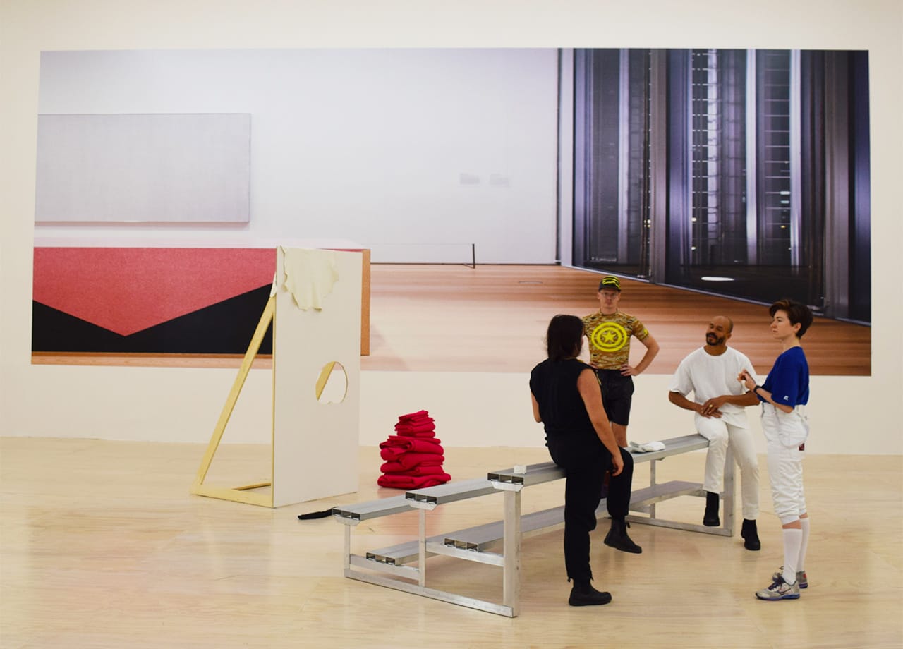 Choreographer Jen Rosenblit and her dancers rehearsing her performance piece "Clap Hands" beneath a large formica piece by Louise Lawler.