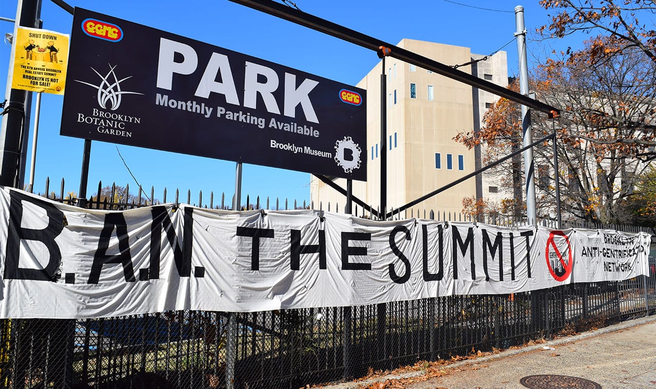 Protesters hung a banner on the fence of the Brooklyn Museum parking lot during the 2015 Brooklyn Real Estate Summit.