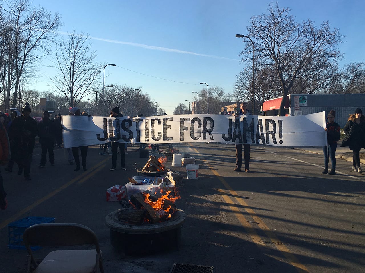 Black Lives Matter Minneapolis activists at the North Minneapolis encampment hold up a banner printed with artist Piotr Szyhalski’s printing tools. (photo by Sam Gould)