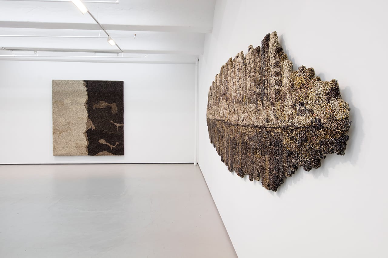 Installation view, 'Vibha Galhotra: ABSUR –CITY –PITY -DITY' at Jack Shainman Gallery, with (left to right): "Untitled" (from the 'Flow' series, 2013), metal ghungroos on fabric stretched over wood panel, 95 x 87 x 3 inch; and "Majnu Ka Tila" (2015), nickel coated ghungroos, fabric, wood, polyurethane coat, 52 x 178 x 2 in (click to enlarge)