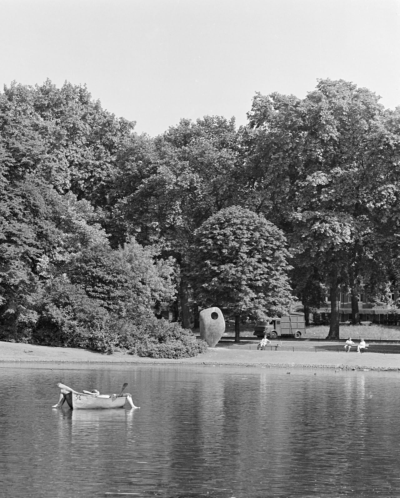 a rowing boat on the boating lake at battersea park with legs sticking out of it, ripples on the water and the sculpture 'single form' by barbara hepworth in the distance battersea park single form sculpture greater london wandsworth battersea
