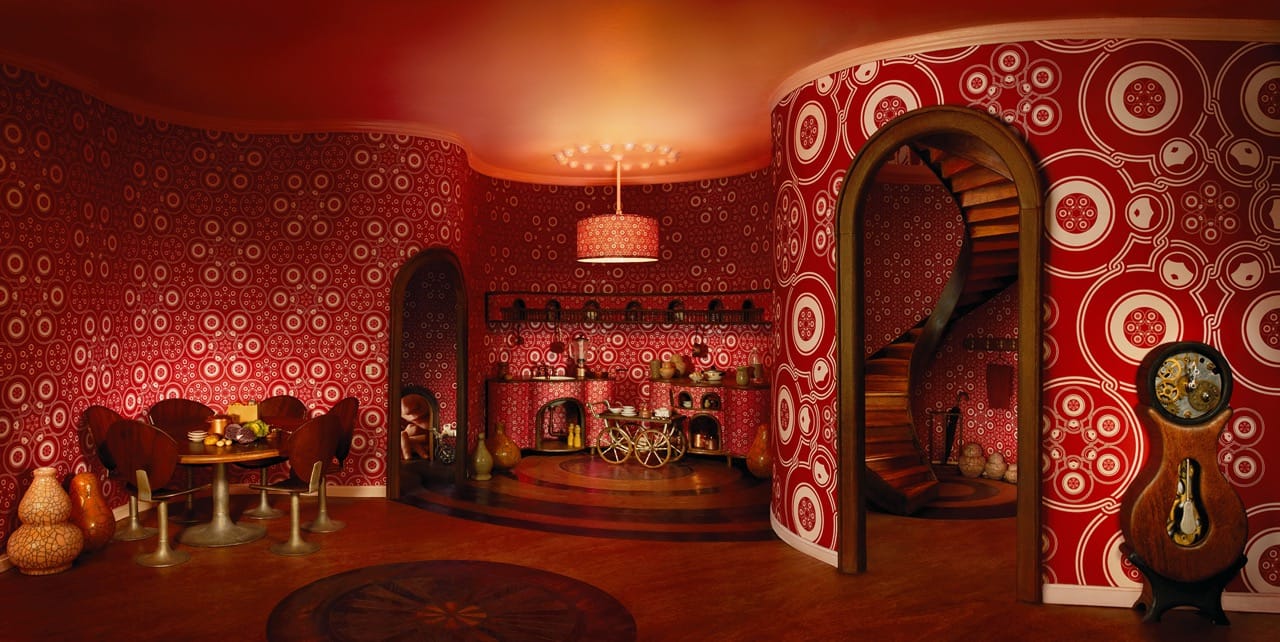 The Fractal Architectures SeriesBuilding the imageThe Fractal Architectures, is a series of nine images divided into three chapters: The Matryoshka Dolls, The Square Roots, and The Star Shells. The hyper-realistic models, conceived for the unique point of view of the camera, are built in the toy scale of 1/24 to life size and above, following a fractal logic. Within the interlocked spaces, body parts such as a foot, a thumb or a face appear to reveal the multiple scales incorporated in the model. Young characters unfold within these fractal architectures, which are at once their toy, their home, their childhood, their adulthood, the space between their past and their future. After the photograph is realized each of these miniatures is deconstructed.Fractal GeometryThe conception of each model begins with a simple geometric figure; the circle for the Matryoshka Dolls, the square for the Square Roots, and the spiral for the Star Shells. These elementary forms repeat at different scales to create an intricate pattern, which weaves together the infinitely small and the infinitely big. This never-ending fractal motif spreads across the wallpaper, and is the basis of the model’s floor plan and interior design. The Matryoshka DollsThe first chapter of the Fractal Architectures unfolds the archetype of the circle. The wallpaper for the Matryoshka series is made up of nested dolls woven in a circular dance, each impregnated with this repeating pattern. Similarly in the model, the circular archetype puts everything in rotation; the hardwood floor grows in concentric circles, the doors bend in arches, and the staircase swirls to the higher alcoves. The walls undulate organically, folding and refolding in a womb-like interior where the exterior seems to no longer exist.