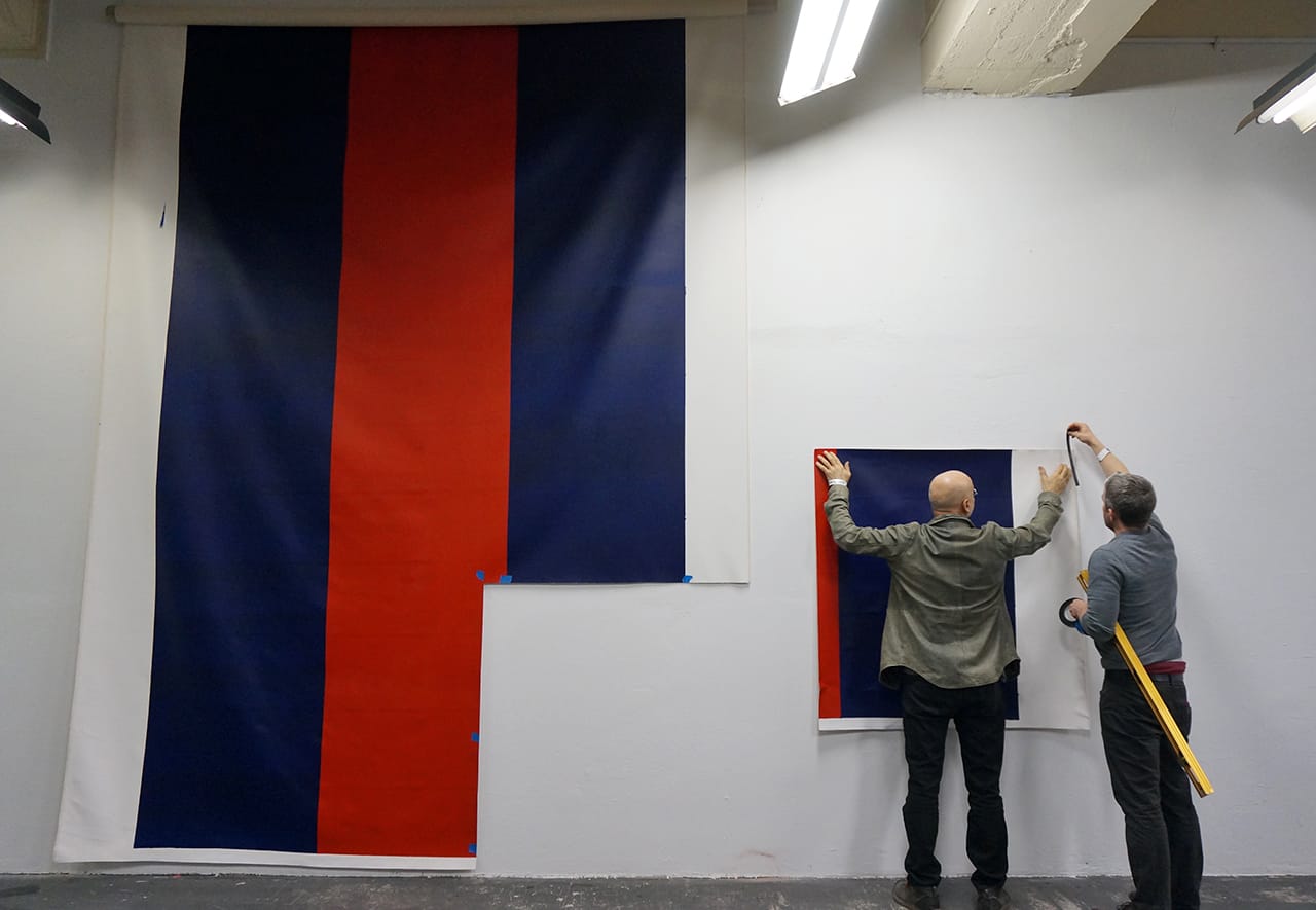 Tamas Banovich and William Powhida hanging up the chopped piece of the faux "Voice of Fire"