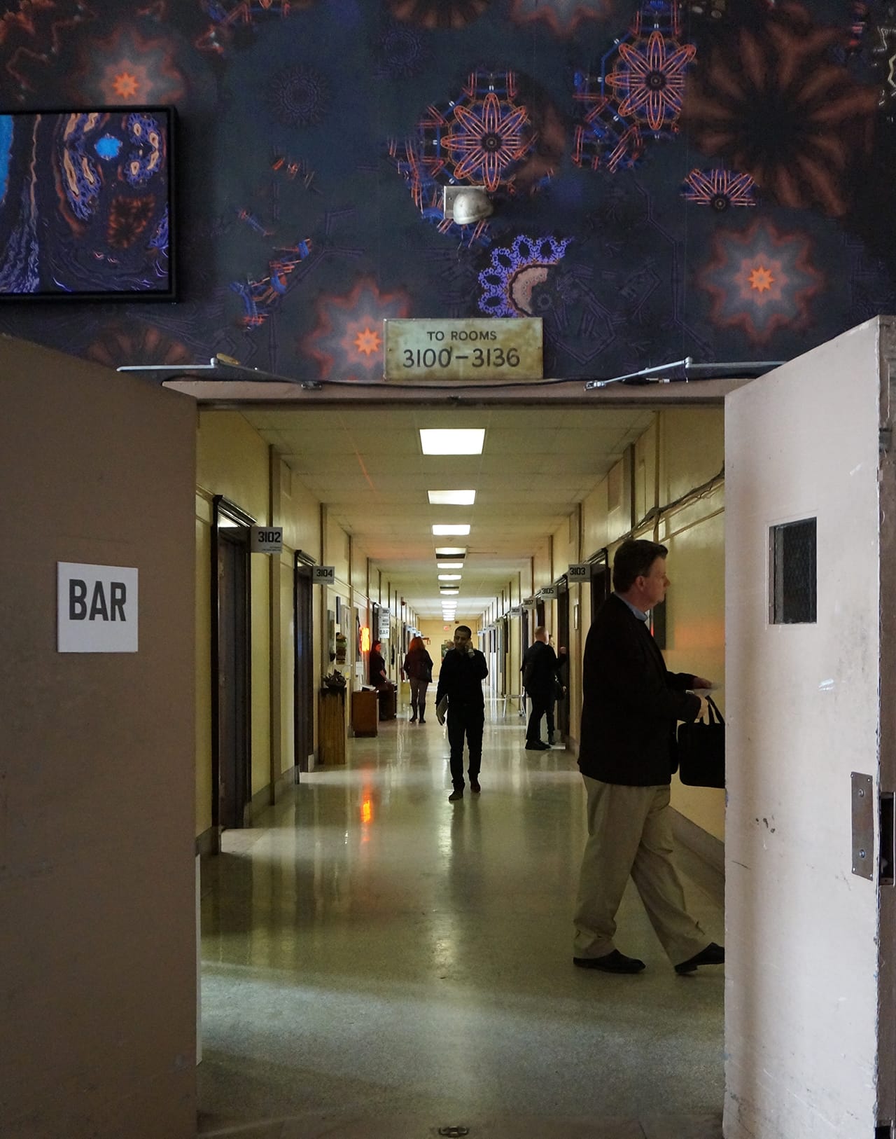 One of the hallways of the 2016 Spring/Break Art Show, housed in the Skylight at Moynihan Station. Across the top is a piece of Anne Spalter's allover lobby mural "Precession." (all photos by the author for Hyperallergic)