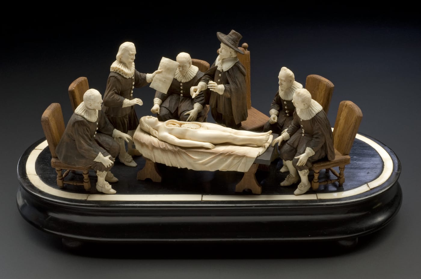L0057499 Wood and ivory figure group representing an anatomical demon Credit: Science Museum, London. Wellcome Images images@wellcome.ac.uk http://wellcomeimages.org Wood and ivory figure group representing an anatomical demonstration by Nicholis Tulp, based on Rembrandt's painting "The Anatomy Lesson". Full view, graduated matt black perspex background. Published: - Copyrighted work available under Creative Commons Attribution only licence CC BY 4.0 http://creativecommons.org/licenses/by/4.0/