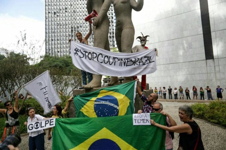 Protesters climb a sculpture in Rio de Janeiro with signs that say “Stop Coup in Brazil” and “Out Temer” (courtesy Ocupa MinC RJ)