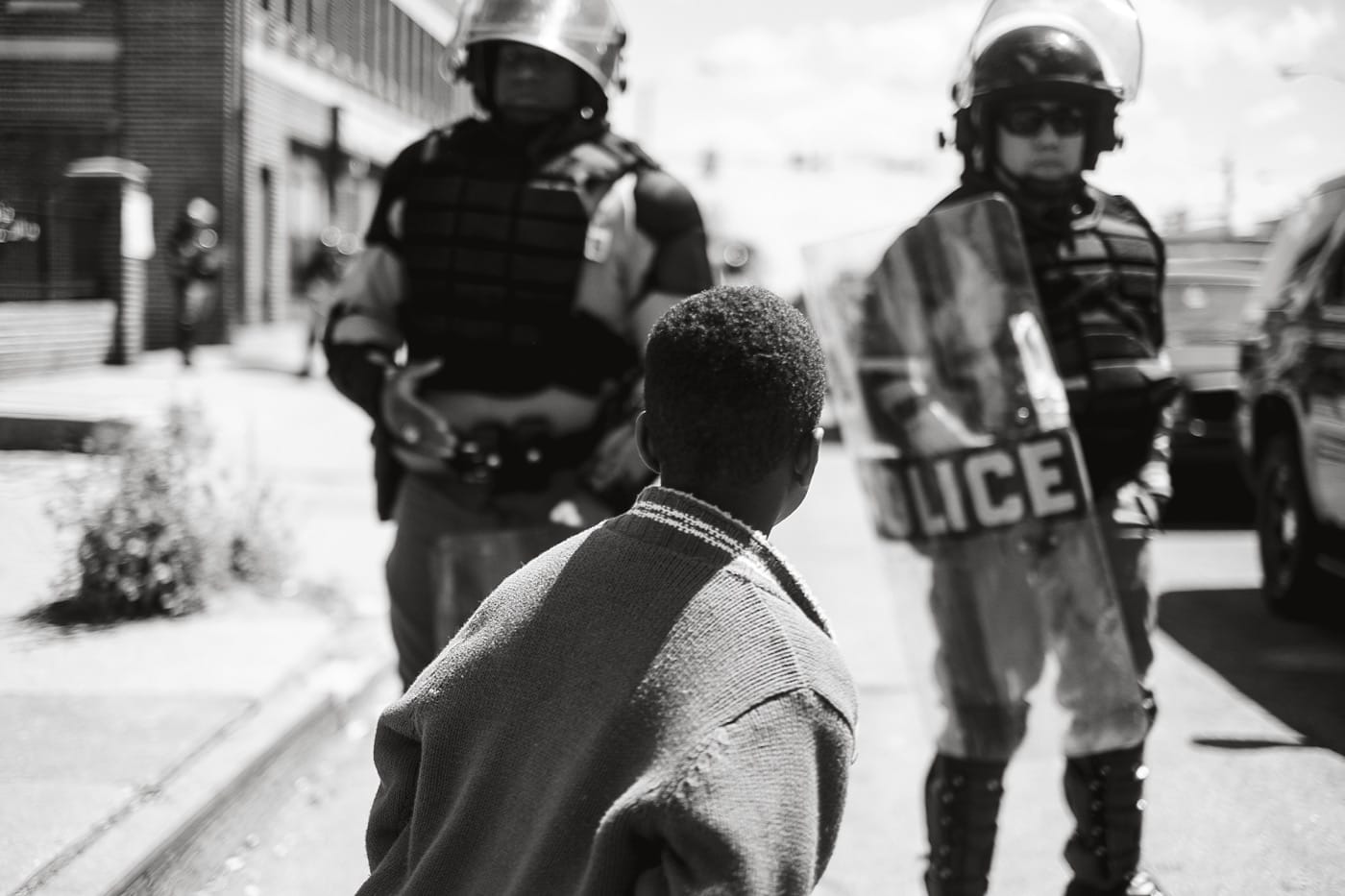 Devin Allen, "Young boy standing in front of police officers at a blockade, North Avenue, West Baltimore" (2015). (All photos courtesy of the artist and Aperture Magazine)