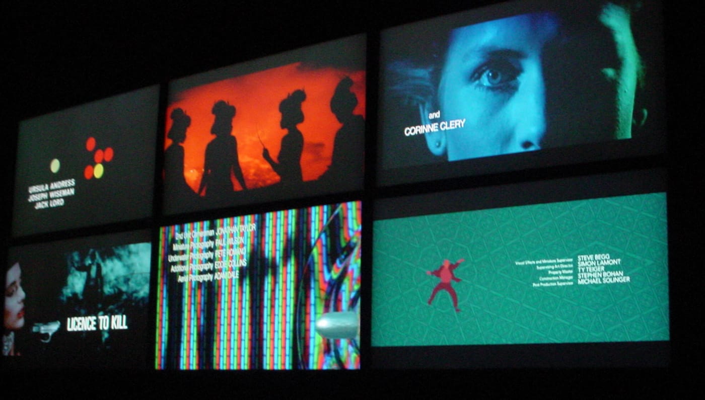 Six screens playing opening title sequences from various James Bond films (photo by the author for Hyperallergic)
