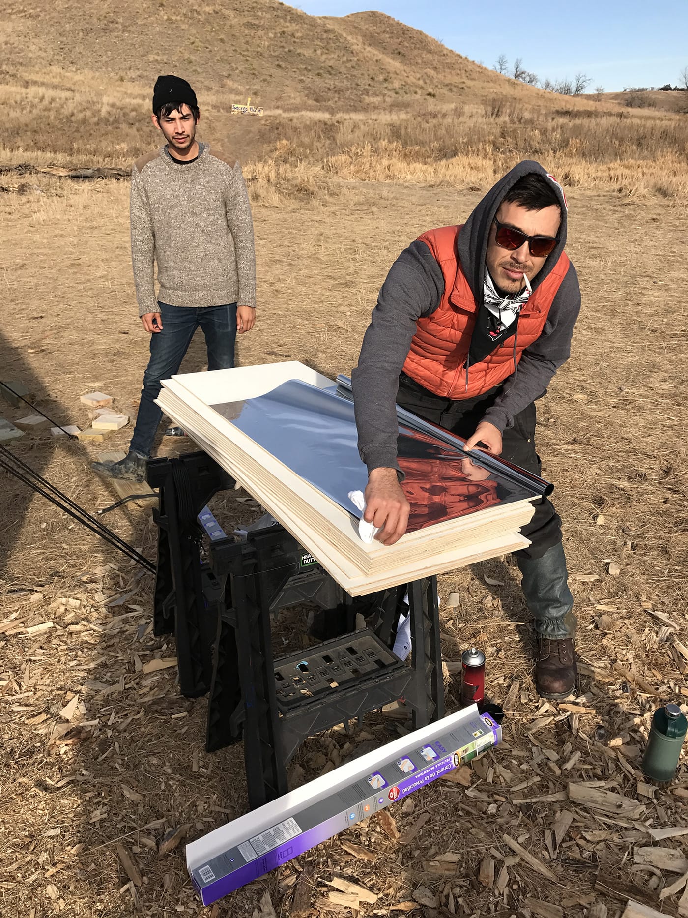 Artist Cannupa Hanska Luger working on a mirrored shield with artist Dylan McLaughlin in the background.