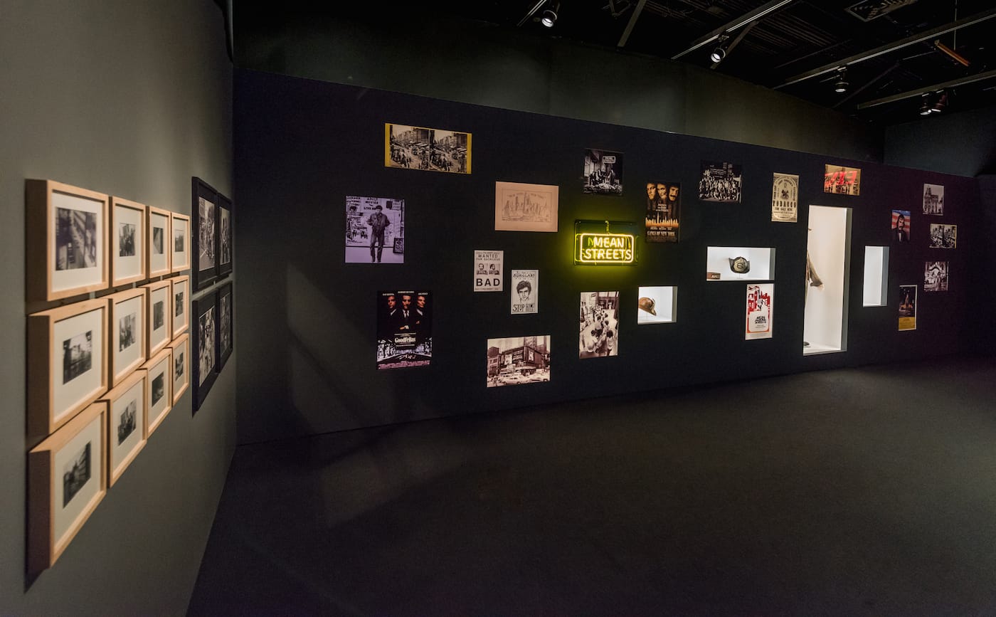 A wall of marketing images relating to New York City-set movies directed by Martin Scorsese, with props and a costume from <em/>Gangs of New York (2002) inset in alcoves for <em>Martin Scorsese</em> at the Museum of the Moving Image (photo by Thanassi Karageorgiou, courtesy the Museum of the Moving Image)