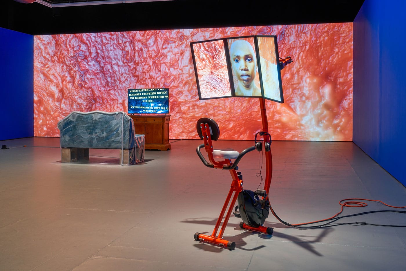 From right to left: Sondra Perry, "Graft and Ash for a Three Monitor Workstation" (2016), video, bicycle workstation, 9:05 min; "Resident Evil" (2016), 3D animation created with Blender open-source software, video on monitor on credenza, 17:29 min; "Historic Jamestowne: Share in the Discovery and Take Several Seats" (2016), used couch, S Curl Activator, spray paint, vinyl cover, cinder blocks 