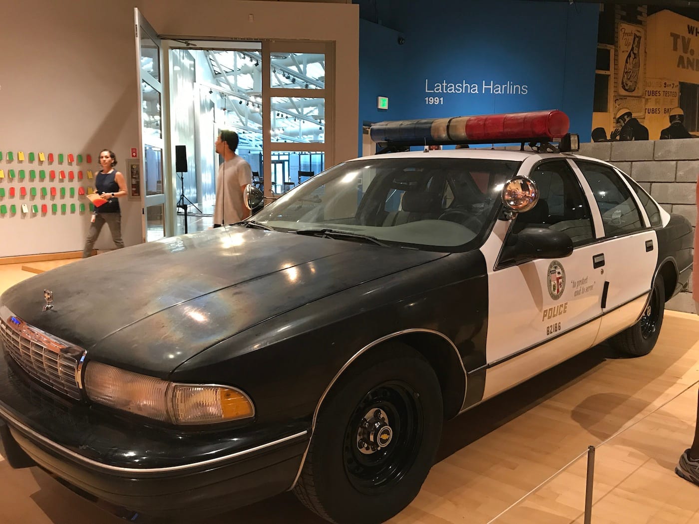 A 1990s police car ominously sits in the back of the exhibition space in No Justice, No Peace: LA 1992 at the California African American Museum.