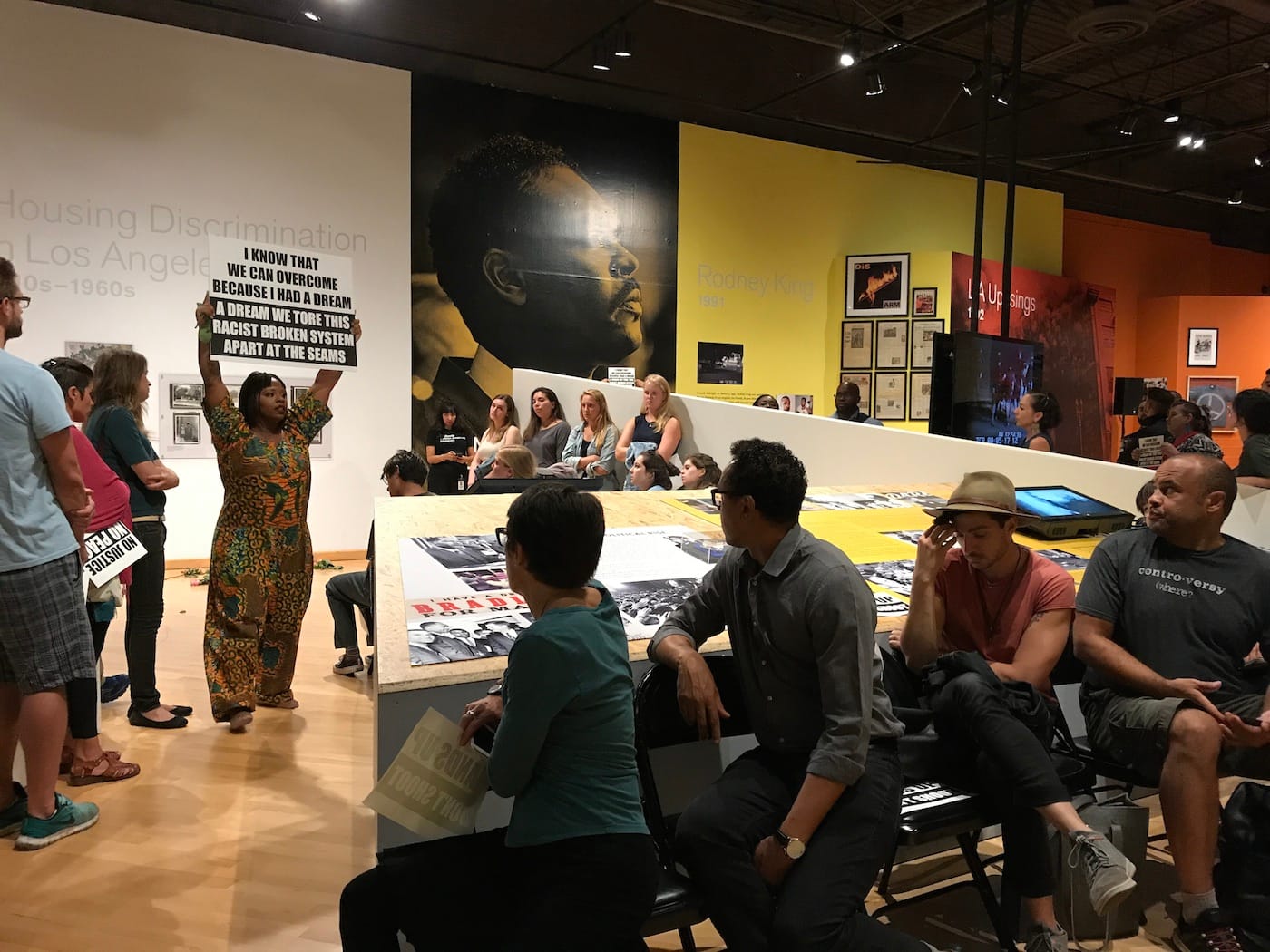 Patrisse Khan-Cullors walks around <em/>No Justice, No Peace: LA 1992 holding various protest signs. (all photos by the author for Hyperallergic)