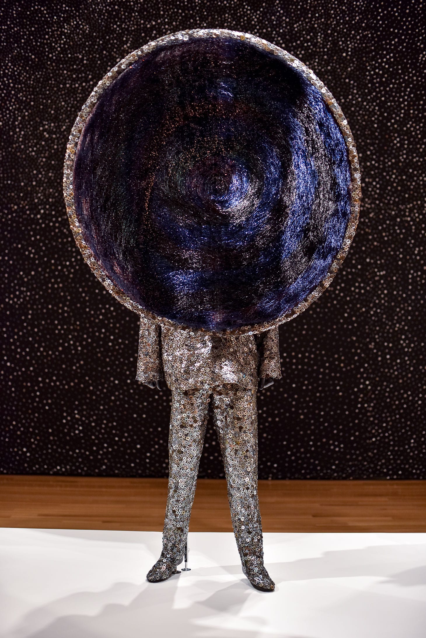 Nick Cave, “Soundsuit” (2018), mixed media including buttons, wire filter head, metal and mannequin, approximately 91 x 51 x 22 inches in front of “Architectural Archway (Button Walls)” (2013)  in mixed media,  288 x 900 inches (image courtesy Akron Art Museum)
