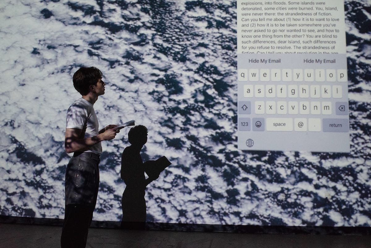 Drew Zeiba Bard MFA Writing class of 2024 performing their work “The Mirror”. Drew is reading in front of a black-and-white p