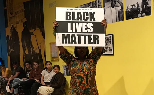 Black Lives Matter co-founder Patrisse Khan-Cullors holds a protest sign during her performance "Remembering '92."